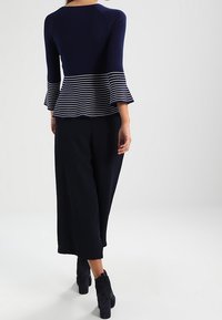Haut en maille bleu marine avec ourlet peplum rayé ; manches évasées. Associé à un pantalon noir à jambes larges et des bottines à talons noires. Texture lisse dans l'ensemble.