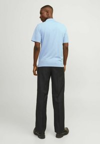 Világoskék rövidujjú pólóing, fekete nadrággal és fekete cipővel párosítva. Az ing klasszikus gallérral és sima textúrával rendelkezik.