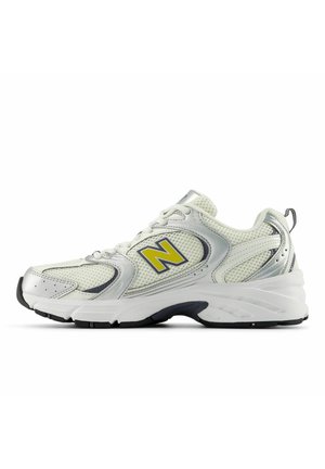 Baskets sportives blanches et argentées avec détails en mesh, logo "N" jaune sur le côté, semelle noire et blanche, et languette à l'arrière.