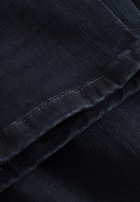 Temno modro denim blago z gladko teksturo, prepognjeno z vidnim šivanjem ob robu, ki prikazuje čist in enakomeren videz.