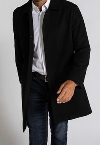 Cappotto di lana nera con frontale abbottonato, colletto e tasche laterali. Abbinato a una camicia bianca e jeans scuri, mette in risalto una silhouette slanciata.