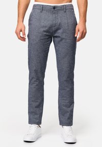 Pantalones grises texturizados con un ajuste entallado, que presentan un diseño de frente plano, pasadores para cinturón y un cierre de un botón, combinados con zapatillas blancas.