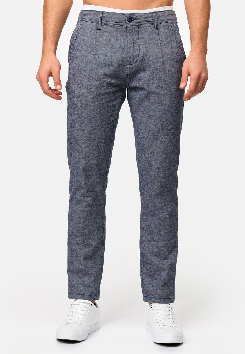 Pantalones grises texturizados con un ajuste entallado, que presentan un diseño de frente plano, pasadores para cinturón y un cierre de un botón, combinados con zapatillas blancas.