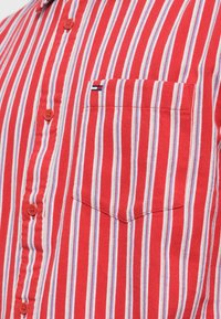 Rød- og hvitstripet skjorte med knapper, med lomme på venstre bryst og lite logo, laget av teksturert bomullsstoff.