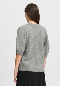 Grå stickad tröja med korta ärmar, ribbad halsringning och nederkant, med en mjuk textur och avslappnad passform. Baksidan visar sömdetaljer.