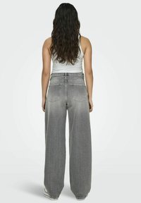Bredde ben grå denimbukser med en falmet finish, to baklommer og høy midje. Brukt med en hvit tank topp.