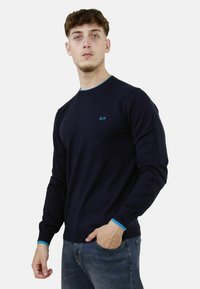 Maglione a maniche lunghe blu navy con colletto e polsini in contrasto di un leggero blu chiaro, con un piccolo logo sul petto. Tessuto morbido, design aderente.
