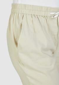 Lichtbeige broek met een elastische tailleband, voorzien van een trekkoord, zijzakken en een gladde textuur. De pasvorm is los en comfortabel.