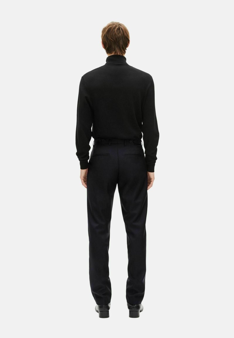 Black turtleneck sweater and dark trousers worn together. The outfit features a fitted design with a smooth texture and minimal detailing.