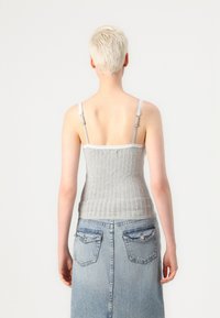 Débardeur en tricot gris avec des bretelles en dentelle, présentant une texture côtelée. Associé à une jupe en denim taille haute, de couleur bleu clair avec des poches arrière.