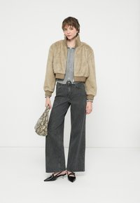 Chaqueta bomber de piel sintética beige, suéter gris de canalé, jeans de pierna ancha con estampado negro, zapatos planos negros de punta y bolso de estampado de serpiente.