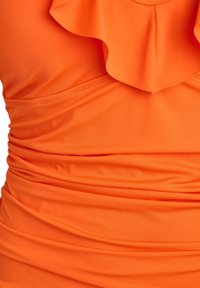 Oranžový plavkový top s volánovým výstrihom, zberanou tkaninou a hladkým povrchom s jemným prešívaním.