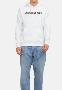 Hvid bomulds hoodie med en frontlomme, snoretræk og et sort logo-print. Samlet med lyseblå jeans med buede sømme.