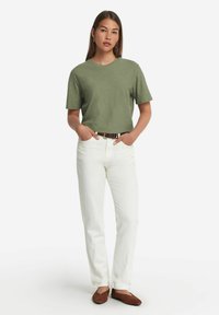 Olivgrön t-shirt med korta ärmar, i kombination med vita högmidjade jeans och bruna platta skor. Texturerad tyg med avslappnad passform.