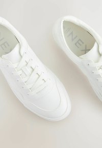 Sneaker bianche realizzate in materiale sintetico liscio, con un design con lacci, punta rotonda e suola testurizzata. Logo del marchio discreto sulla soletta.