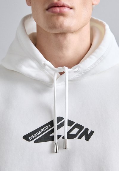 Sudadera blanca con un logo impreso en negro "DSQUARED2 ZCN" y puntas plateadas en los cordones, que exhibe una textura suave y un diseño casual.