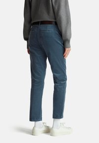 Blaue Cordhosen mit enger Passform, die eine glatte Textur und zwei Gesäßtaschen aufweisen. Getragen mit weißen Sneakers und knöchellangen Socken.