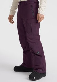 Violet lumppuhousut monien taskujen kanssa, vetoketjuyksityiskohta reisissä, säädettävät hihnat ja logopatchi alaosassa.