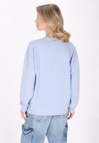 Felpa oversized blu chiaro con polsini e orlo a coste, caratterizzata da una texture liscia e spalle drop, indossata con pantaloni cargo blu chiaro.