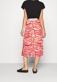Röd och beige zebra-randig kjol i midilängd med en framfalsk, med en Calvin Klein-logotyp på midjeresåren. Parats med svarta slidesandaler.
