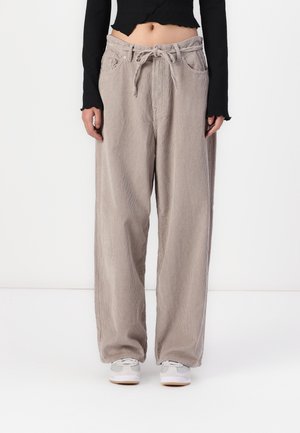 Persona que lleva pantalones anchos de pana color beige con cintura de cordón, un top negro corto de manga larga y zapatillas blancas.