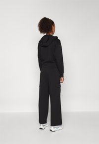 Black cotton hoodie with a kangaroo pocket and hood, paired with wide-leg black cargo pants featuring side pockets. Worn with white sneakers.