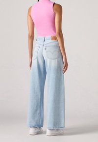 Jasnoniebieskie dżinsy typu wide-leg z delikatnym odcieniem, z klasycznymi tylnymi kieszeniami i brązową skórzaną metką na pasie.