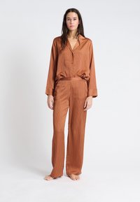 Roodkleurige satijnen pyjamaset met verticale witte strepen. Het shirt heeft een kraag en knopen; de broek is losjes passend met een elastische tailleband.