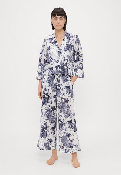 Pamučni pidžama set s bijelom pozadinom i plavim cvjetnim uzorcima. Sadrži košulju s ovratnikom i hlače širokih nogavica, obje opuštenog kroja.