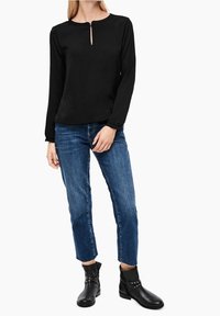 Svart långärmad topp med rund halsringning och nyckelhålsdetalj, kombinerad med blå cropped jeans och svarta ankelstövlar med nitar.