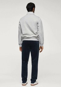 Sweat-shirt gris à col montant et ourlet côtelé, associé à un pantalon en velours bleu marine et des baskets blanches, vu de dos.