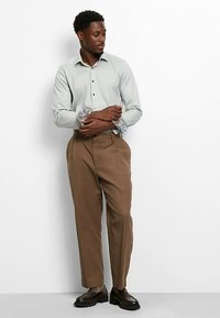 Hellgraues langärmliges Hemd mit gemusterten Manschetten, kombiniert mit braunen, plissierten Hosen und schwarzen Schuhen. Glatter Stoff, lockere Passform.