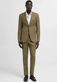 Olive green suit with a tailored fit, featuring a notch lapel, two buttons, and a white shirt. Brown shoes complete the look.
