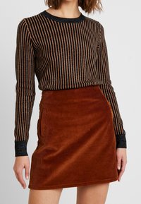 Zwarte en bronzen gestreepte lange mouw top met glinsterende accenten, gecombineerd met een bruine corduroy mini rok met zijzakken.