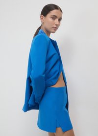 Blauer, maßgeschneiderter Blazer und Minirock aus glattem Stoff. Der Blazer hat eine offene Vorderseite mit tailliertem Schnitt und der Rock ist mit einem hohen Schlitz versehen.