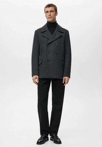 Abrigo corto cruzado de lana gris oscuro con cuello con muescas, bolsillos laterales y tejido texturizado, llevado sobre un suéter de cuello alto negro y pantalones negros.