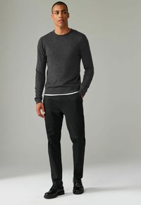 Mørkegrå crew-neck sweater lavet af strikket stof, parret med sorte bukser og sorte snørebåndssko. Modellen står med hænderne i lommerne.