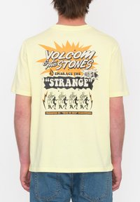Camiseta de algodón amarilla con un diseño gráfico que presenta el texto "VOLCOM & THE STONES" y un motivo de esqueleto bailando en la parte posterior.