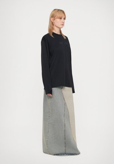 Zwarte langwerpige blouse met een subtiele logo, gecombineerd met een patchwork denimrok met lichte en donkere blauwe secties, vloer-length ontwerp.