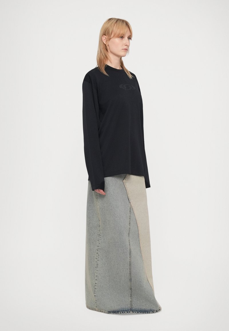 Sort langærmet skjorte med et diskret logo, parret med en patchwork denimskørt, der har lyse og mørke blå sektioner, gulvlængde design.