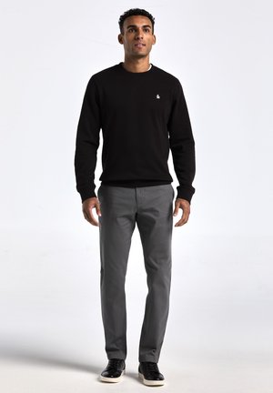Zwarte sweatshirt met ronde hals en ribgebreide boorden, gecombineerd met grijze rechtlopende broek. Zwarte schoenen maken de outfit compleet.