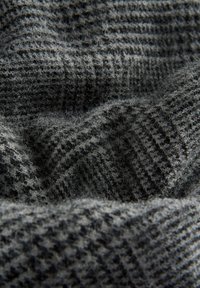 Tissu gris texturé avec un motif à carreaux subtil, doux, légèrement duveteux, et drapé, mettant en valeur différentes nuances de gris dans le tissage.