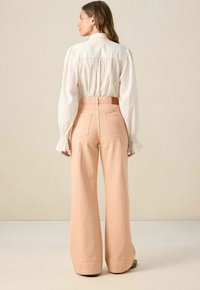 Cream blouse with puffed sleeves paired with light peach wide-leg trousers, featuring back pockets and a belted waist. Simple design.