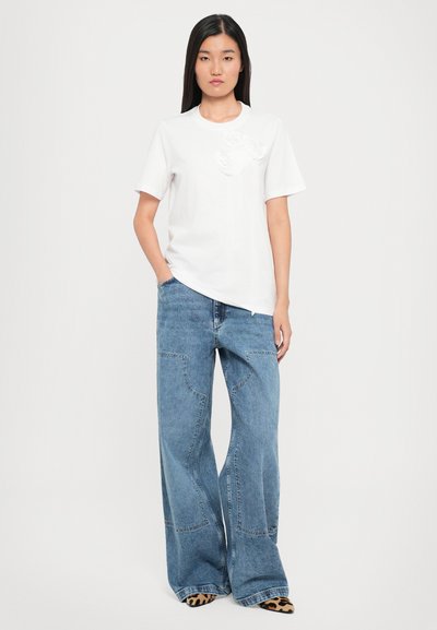 White cotton t-shirt with short sleeves and textured design on the chest, paired with wide-leg blue denim jeans and animal print shoes.