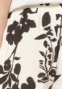Pantaloni floreali con sfondo bianco e grandi motivi floreali marroni. Il tessuto è leggero, con vita elastica e una morbida texture.