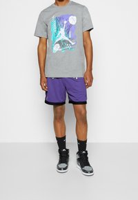Gray graphic t-shirt with a colorful basketball design, paired with purple mesh shorts featuring black trim, and black sneakers.