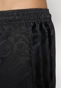 Black athletic shorts featuring a textured floral pattern and satin black side stripes. Elastic waistband for comfort.
