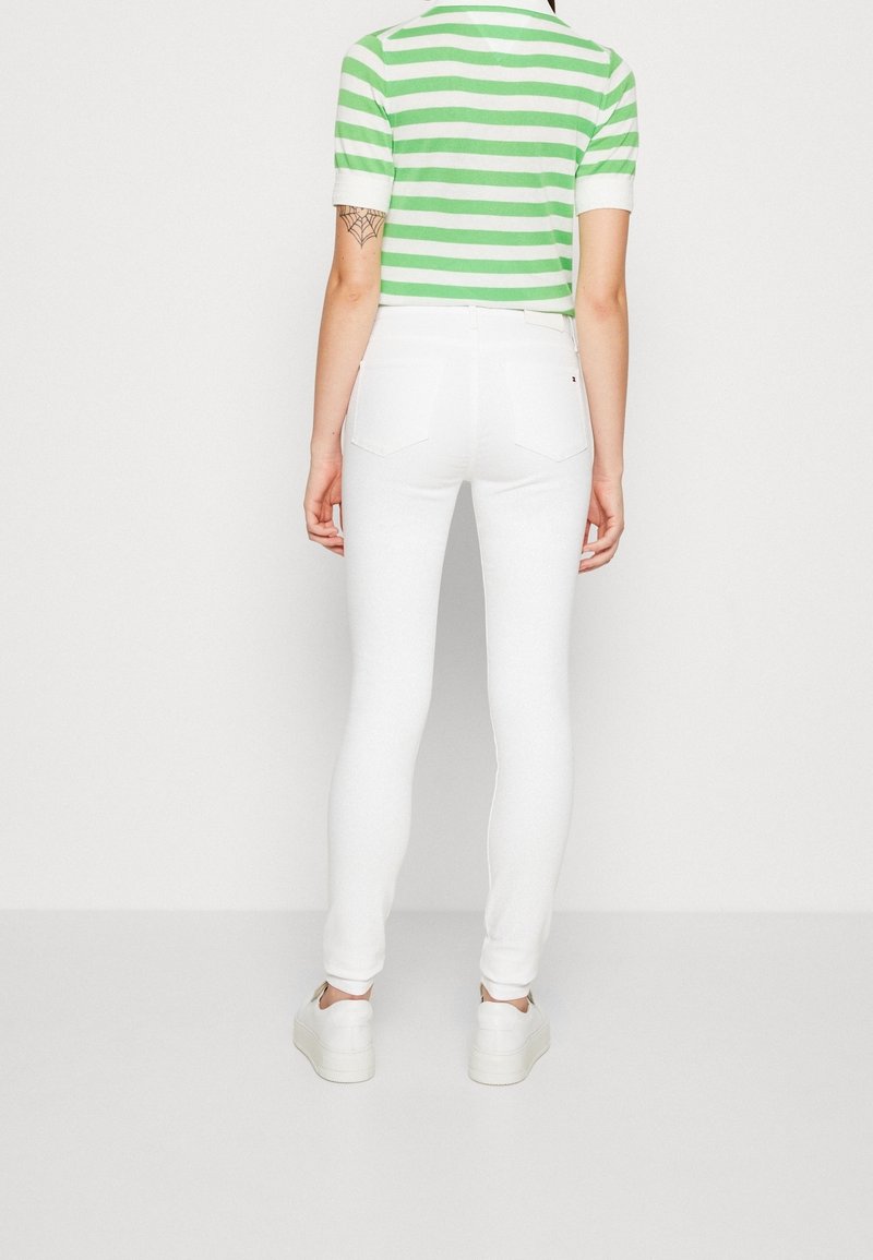 Jeans ajustados blancos con una textura suave, combinados con una camisa polo a rayas en verde y blanco. Los jeans tienen dos bolsillos traseros.