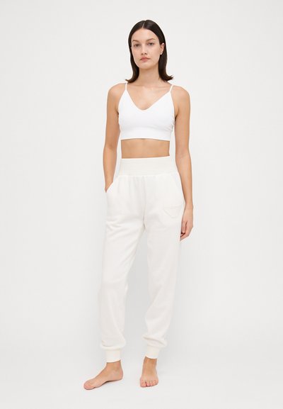 Bralette bianco in cotone con scollatura a V e spalline sottili, abbinato a pantaloni jogger bianchi con vita elastica e un piccolo logo sulla tasca.