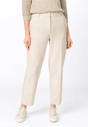 Pantalons beiges ajustés à coupe droite, dotés de poches latérales et d'un tissu lisse et léger. Associés à des baskets blanches.